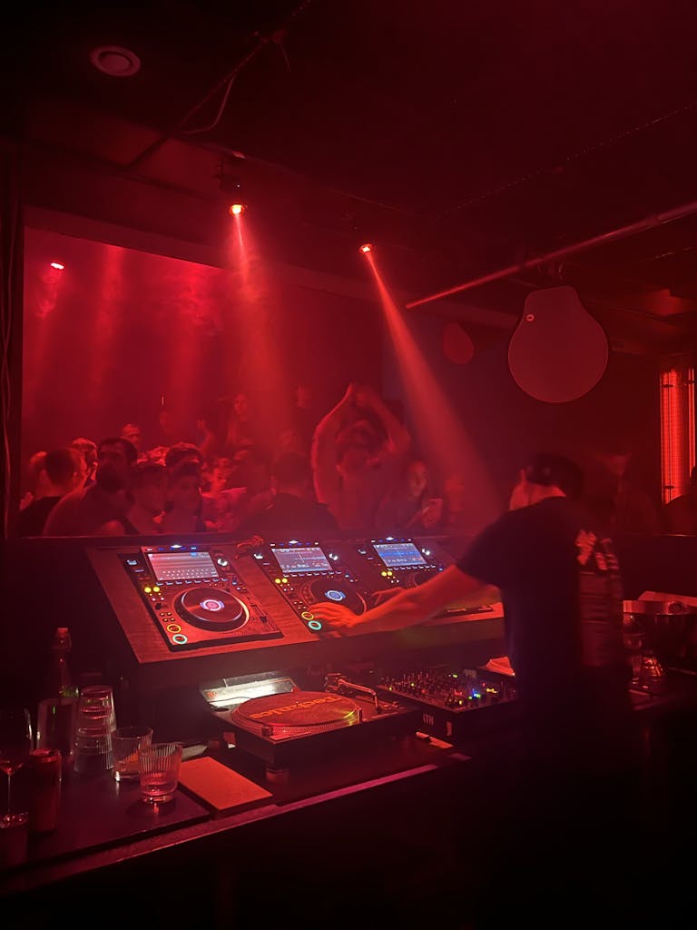 A DJ spins music in a vibrant Stockholm nightclub, filled with a lively crowd under red lighting.