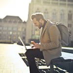 Man working on laptop in Budapest park while enjoying ice cream, showcasing remote work lifestyle.