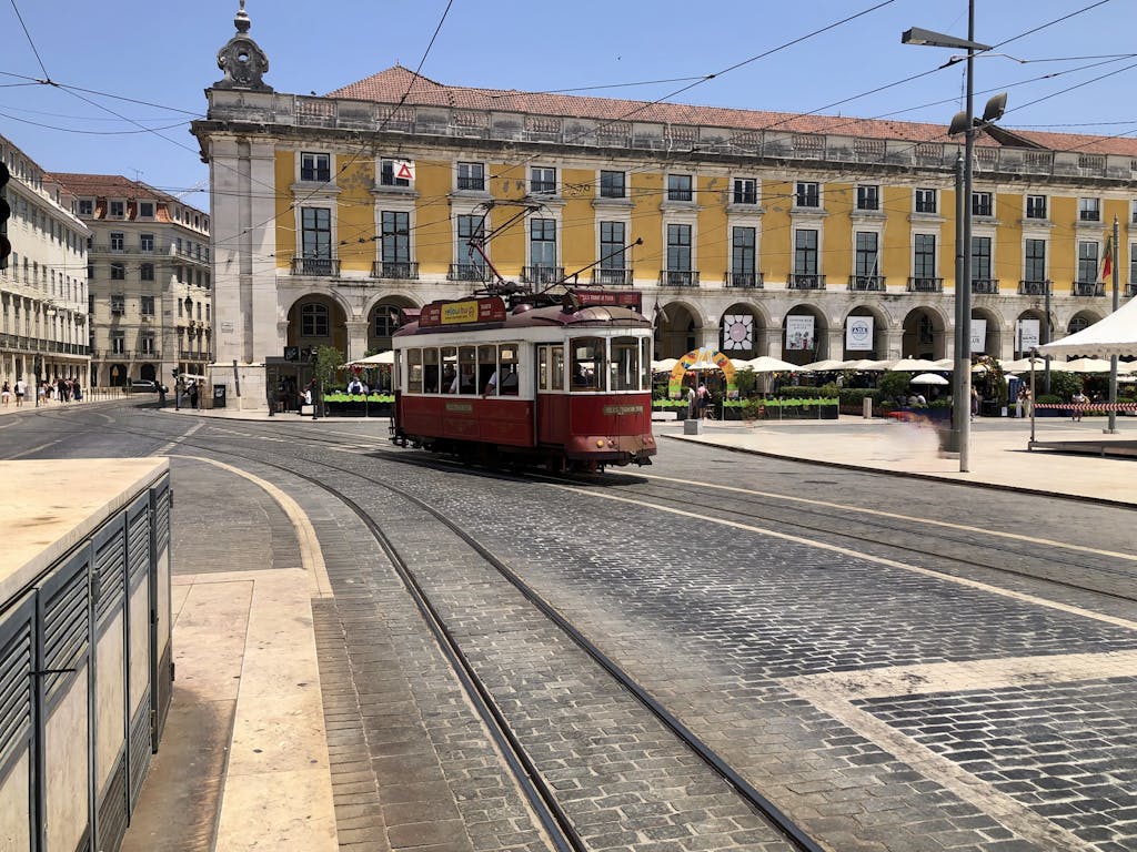 Red tram passing through Comercio Square in Lisbon on a sunny day.
