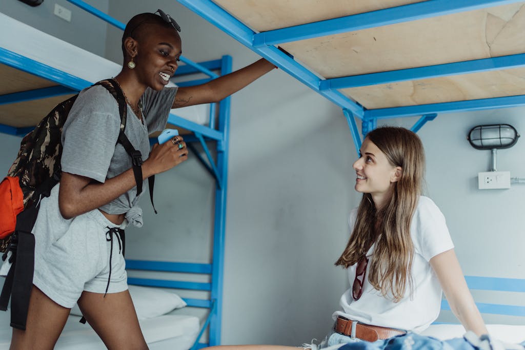 Two women in a hostel room enjoying conversation by the bunk beds.